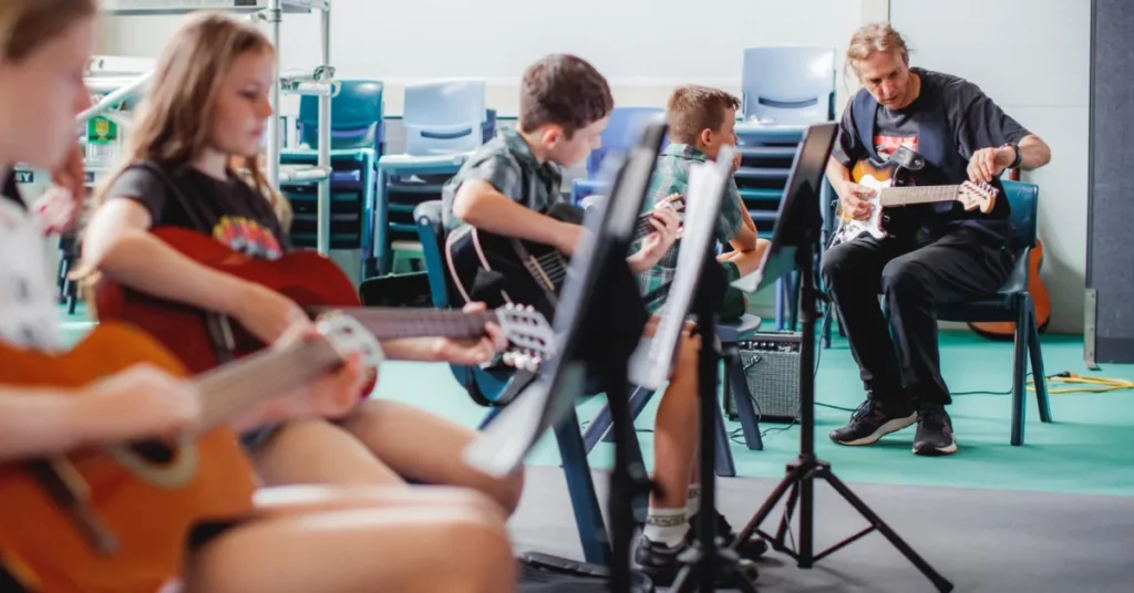 A qualified music teacher Gold Coast instructs a small group of young students learning electric and acoustic guitar on the Gold Coast.